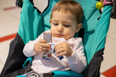 Cute baby girl holding chocolate while sitting in stroller