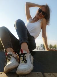 Young woman wearing sunglasses sitting against sky