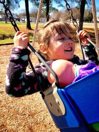 Girl with doll swinging at playground on sunny day