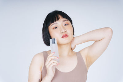 Portrait of young woman holding perfume against gray background