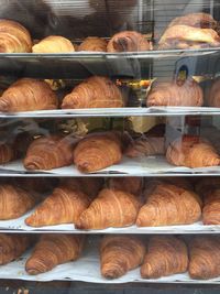 Croissants in cooling rack at bakery store seen through glass window