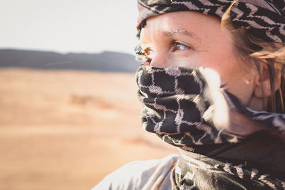 Close-up of woman covering face with scarf in desert against sky