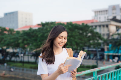 Smiling beautiful woman reading book while standing outdoors