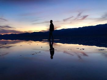 Silhouette man standing in water at sunset