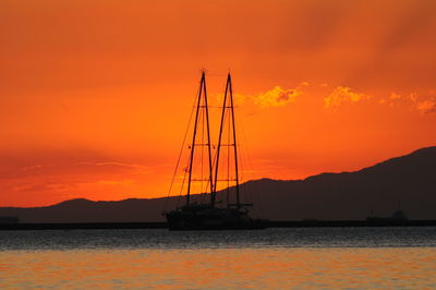 Silhouette sailboat on sea against orange sky