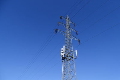 Low angle view of electricity pylon against blue sky