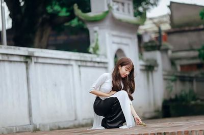 Young woman looking away while sitting on wall