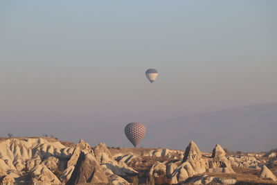 Hot air balloon flying over rocks against clear sky