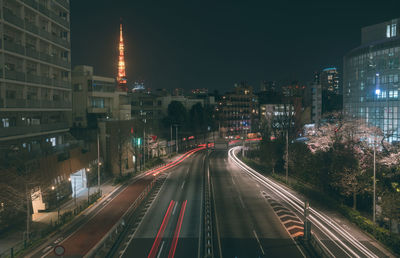 Light trails on road amidst buildings against sky at night