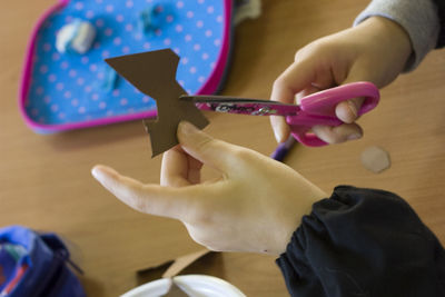 Cropped hands of boys cutting cardboard on table