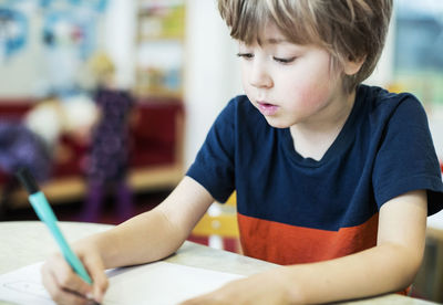 Boy drawing on paper at table in kindergarten