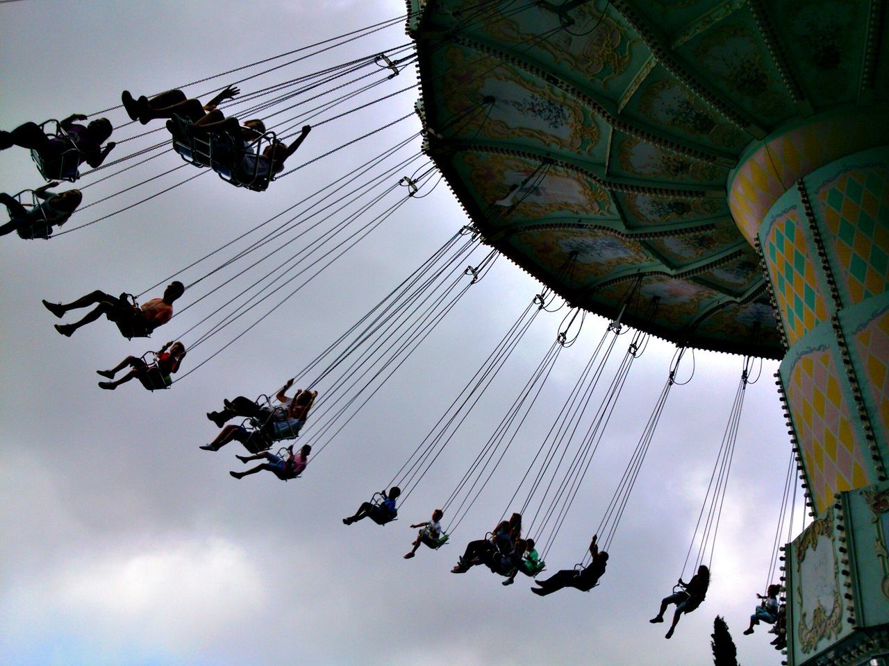 low angle view, arts culture and entertainment, amusement park, sky, amusement park ride, fun, large group of people, enjoyment, leisure activity, silhouette, built structure, architecture, chain swing ride, hanging, ferris wheel, men, lifestyles, outdoors, lighting equipment