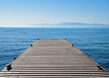 Pier on sea against clear blue sky