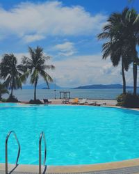 Palm tree by swimming pool against sky