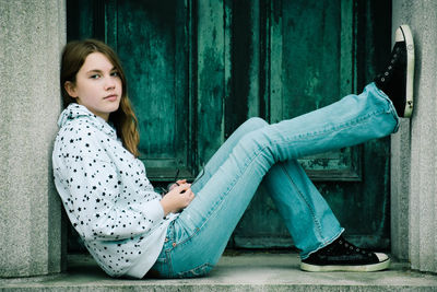 Portrait of a young woman sitting on door