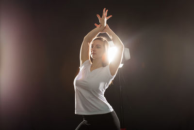 Young woman dancing at studio against black background