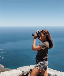 Woman photographing sea against clear sky