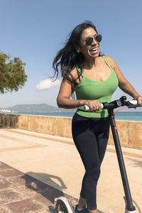 Woman riding electric scooter, happy and summer ride at tropical island beach resort for vacation. 