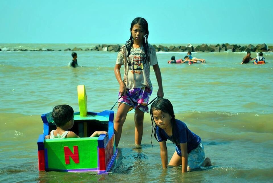 PORTRAIT OF SIBLINGS SITTING ON BEACH