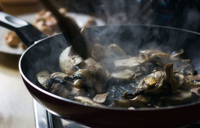 Top view of fresh cut mushroom are being cooked in fry pan with steam coming out and wooden spoon