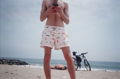 Man holding umbrella on beach against sky