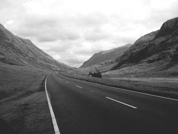 Empty road by mountains against cloudy sky