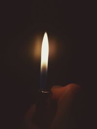 Close-up of hand holding lit candle in darkroom