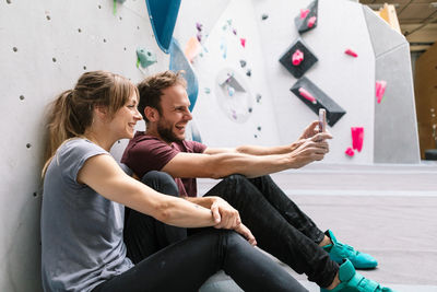 Happy male taking selfie through smart phone with female friend in gym