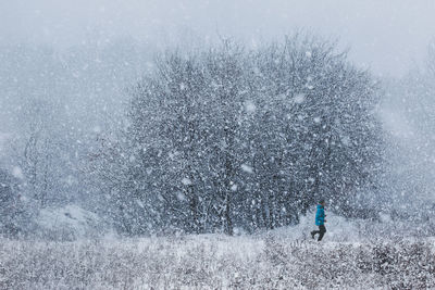 Side view of teenage boy running on field during snowfall in forest