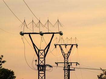 Low angle view of electricity pylon against sky during sunset