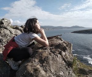 Woman sitting on rock by sea against sky