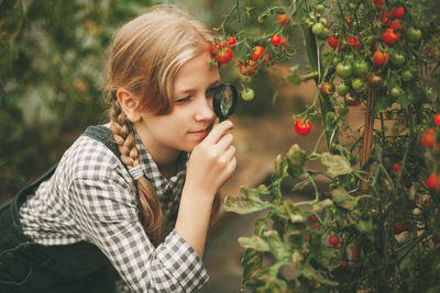 A beautiful little girl examines small cherry tomatoes through a magnifying glass. curious children.