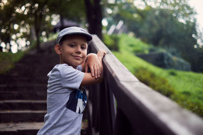 Portrait of smiling boy wearing hat standing by railing on staircase outdoors