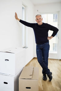 Full length of mature man standing by moving boxes at home