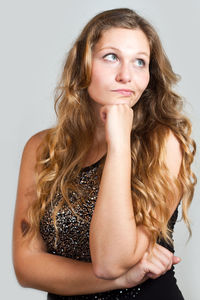 Displeased young woman standing with hand on chin against gray background