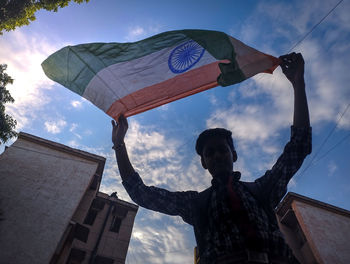 Low angle view of a boy waving indian flag against sky. 