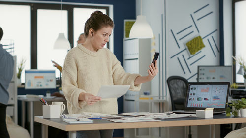 Young woman using mobile phone while standing in office