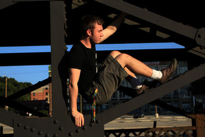 Side view of young man sitting on bridge railing