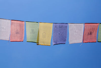 Low angle view of prayer flags hanging against clear blue sky