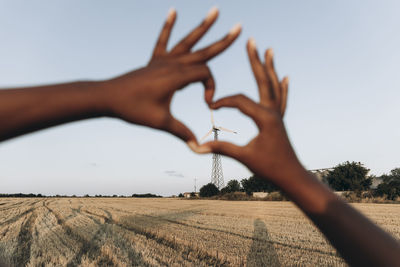 Woman making heart shape with hands in front of sky at farm