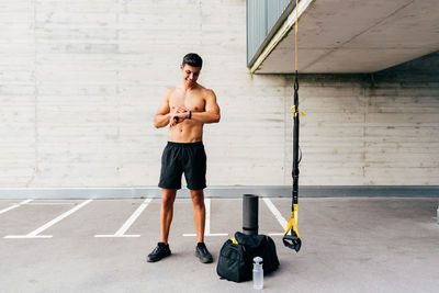 Content shirtless sportsman standing on street and checking pulse on fitness tracker after active workout in city