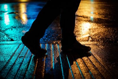 Low section of man standing on wet street at night
