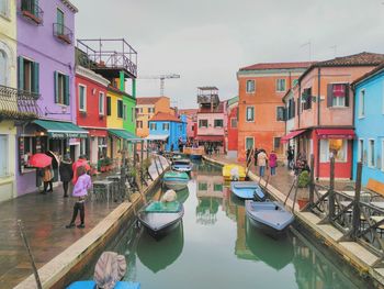 Boats moored in canal amidst buildings in city against sky