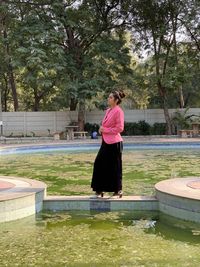 Woman standing by lake against trees