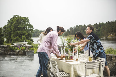 Multi-ethnic friends setting table for dinner party in backyard against clear sky