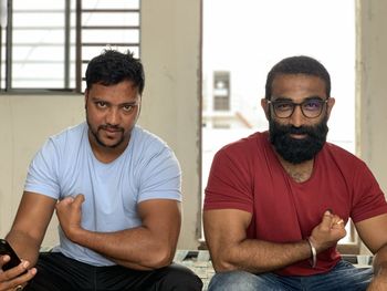 Portrait of friends flexing muscles while sitting indoors