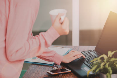 Midsection of woman using mobile phone while sitting on table