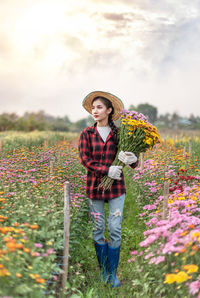 Young woman standing by flower on field against sky