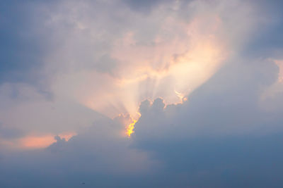 Low angle view of sunlight streaming through clouds during sunset