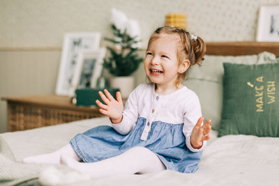 A beautiful little girl is sitting on the bed and laughing, the child is happy about christmas 